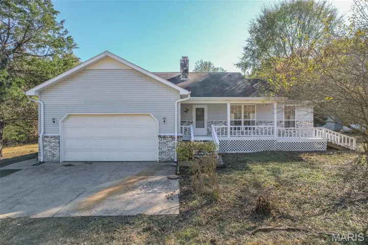 View of front of house featuring a chimney, a porch, an attached garage, and driveway