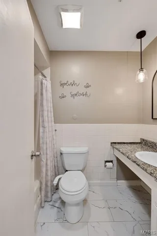 Bathroom with shower / bathtub combination with curtain, vanity, light marble finish floors, tile walls, and a wainscoted wall