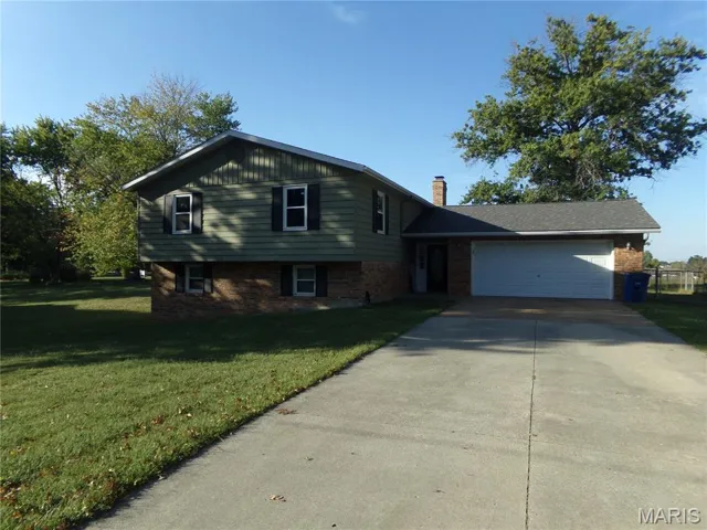Split level home featuring a front yard, concrete driveway, brick siding, a garage, and a chimney
