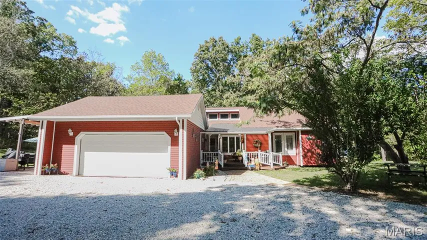 View of front facade featuring gravel driveway, an attached garage, brick siding, and a shingled roof