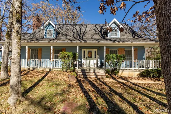 Cape cod-style house featuring covered porch, a shingled roof, and a chimney
