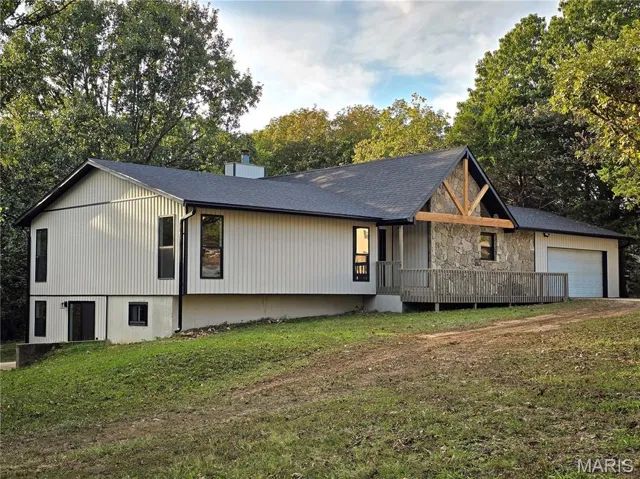 View of front of property featuring a front yard, view of scattered trees, a chimney, a deck, and a garage