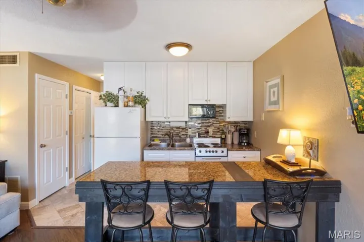 Kitchen featuring a breakfast bar area, decorative backsplash, white appliances, white cabinets, and a textured wall