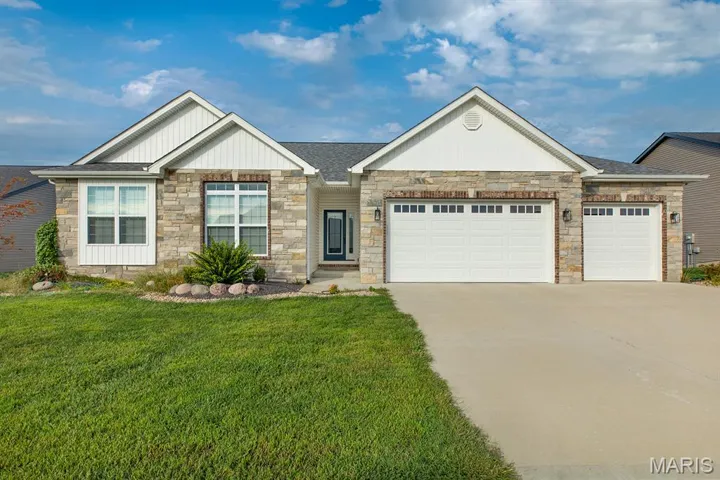 View of front of house with an attached garage, a front lawn, board and batten siding, stone siding, and concrete driveway