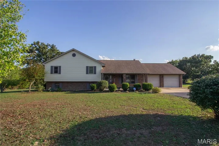 Split level home with brick siding, a front lawn, driveway, and an attached garage