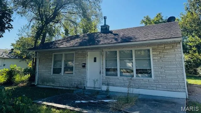 View of front facade with stone siding, a chimney, and a shingled roof