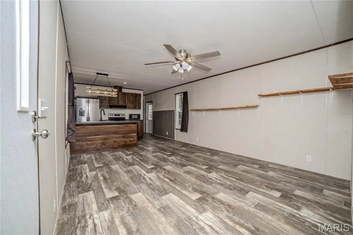 Unfurnished living room with dark wood finished floors, ceiling fan, and a decorative wall