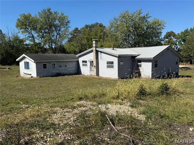 View of front facade featuring a front lawn, a metal roof, and view of scattered trees