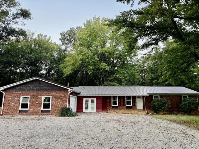 Single story home with an attached garage, a metal roof, and view of scattered trees