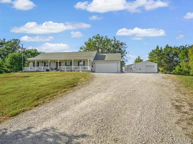 Ranch-style house featuring a porch, a front yard, gravel driveway, and a garage