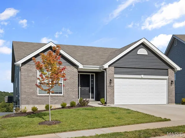 Ranch-style home with a front yard, concrete driveway, an attached garage, brick siding, and a shingled roof