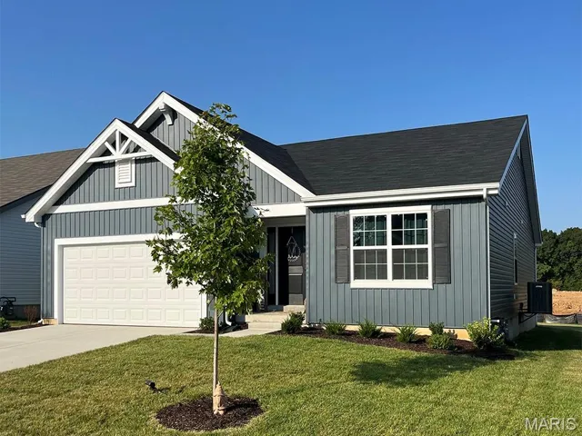 View of front facade with a front yard, concrete driveway, roof with shingles, and a garage