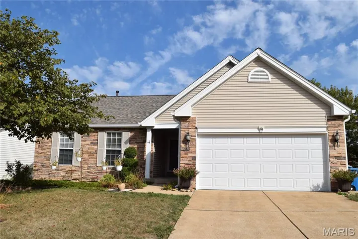 View of front facade featuring stone siding, concrete driveway, a shingled roof, a front lawn, and an attached garage