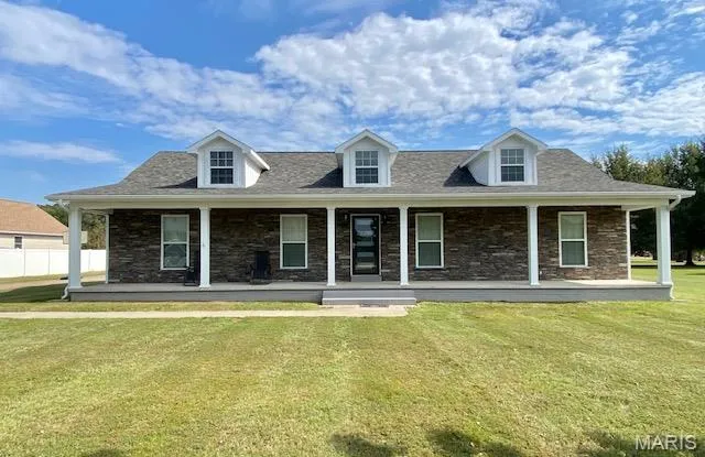 New england style home featuring covered porch, a front lawn, and stone siding