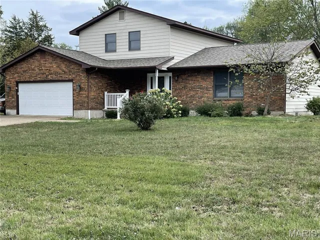 Traditional-style house with roof with shingles, a front lawn, brick siding, and an attached garage
