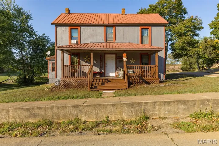 Country-style home featuring a metal roof, a porch, a front yard, and a chimney