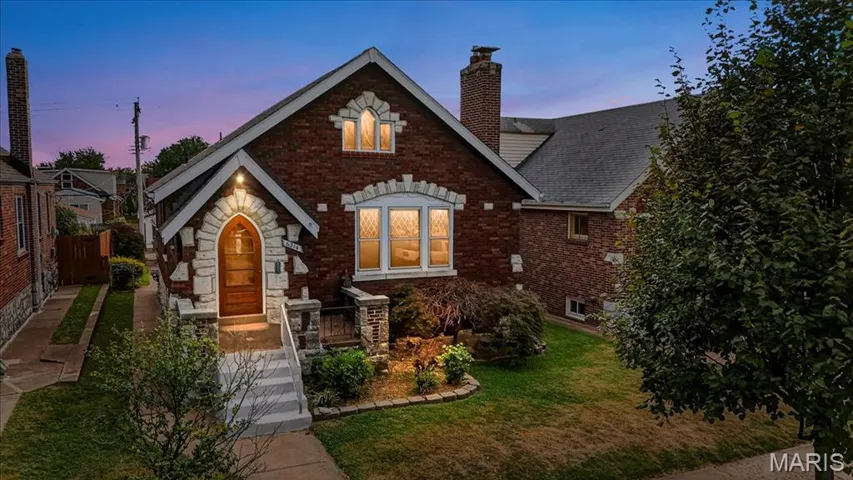 Tudor-style house featuring brick siding, a front lawn, a chimney, a shingled roof, and stone siding
