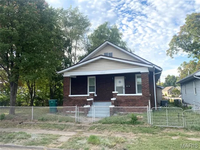 Bungalow-style home featuring a porch, a gate, brick siding, and a fenced front yard