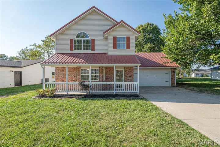 Traditional-style house featuring a metal roof, a front yard, brick siding, and a porch