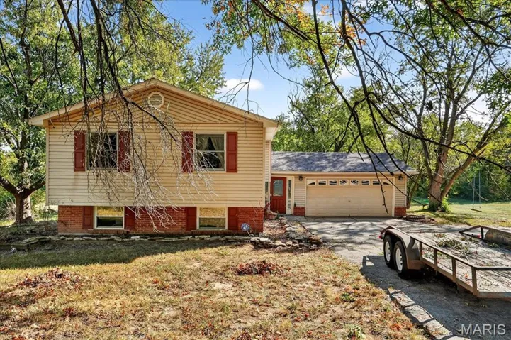 Split level home featuring driveway, a garage, a front lawn, and brick siding
