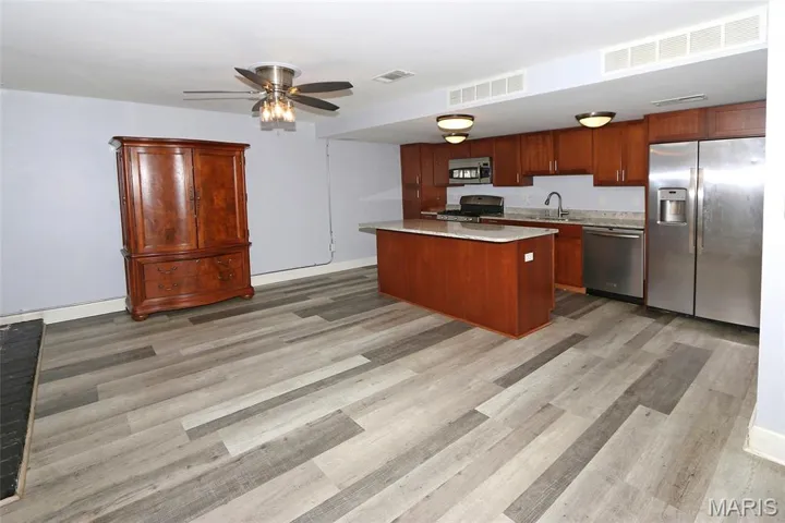 Kitchen featuring appliances with stainless steel finishes, a kitchen island, ceiling fan, light stone countertops, and light wood finished floors