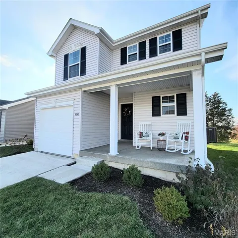 Traditional-style home featuring a porch, a front lawn, a garage, and driveway