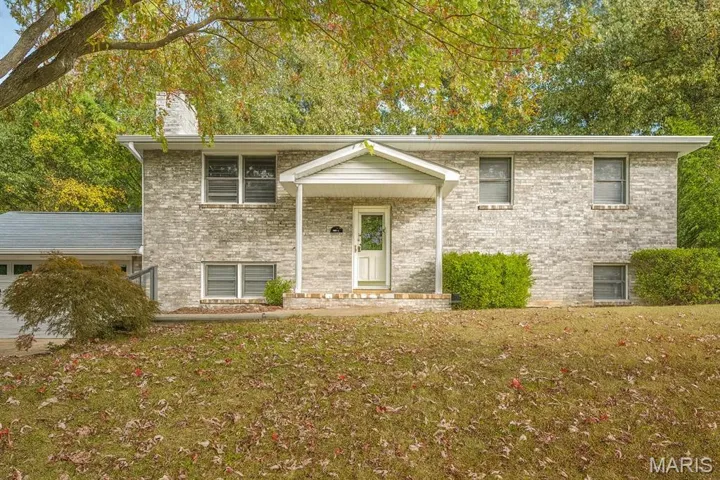 Split level home with a front lawn, brick siding, a chimney, and a porch