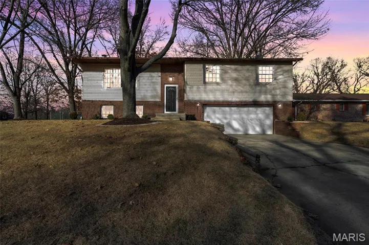 Raised ranch featuring brick siding, concrete driveway, an attached garage, and a front yard