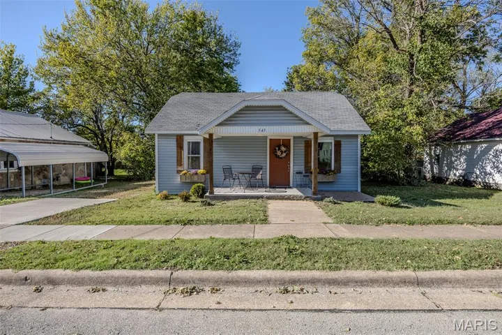 Bungalow-style house with a porch, a front yard, a detached carport, and roof with shingles