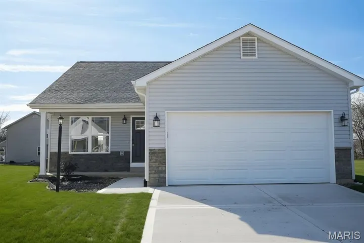 View of front of home featuring driveway, a front lawn, stone siding, and a garage
