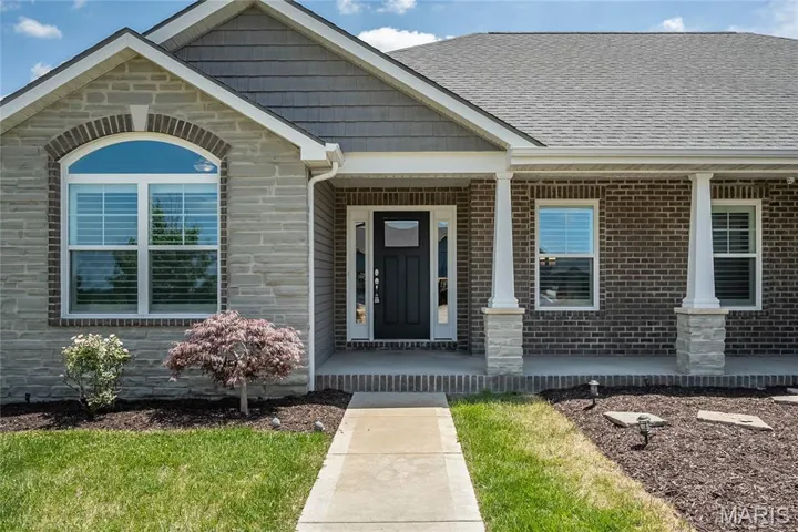 View of exterior entry with covered porch, stone siding, brick siding, and a shingled roof