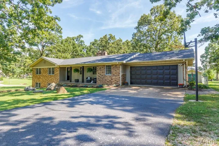 Ranch-style house featuring driveway, a chimney, brick siding, an attached garage, and a porch