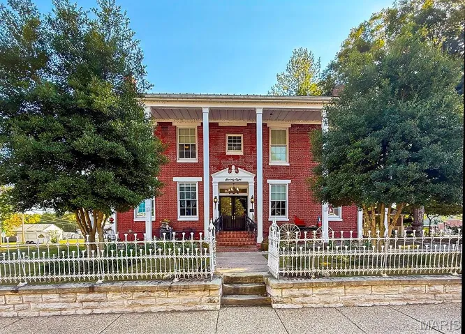 Greek revival house featuring brick siding, a fenced front yard, and covered porch