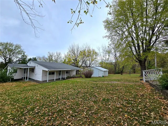 View of green lawn featuring an outbuilding and covered porch