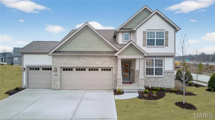 Craftsman-style home with stone siding, a front yard, an attached garage, and concrete driveway