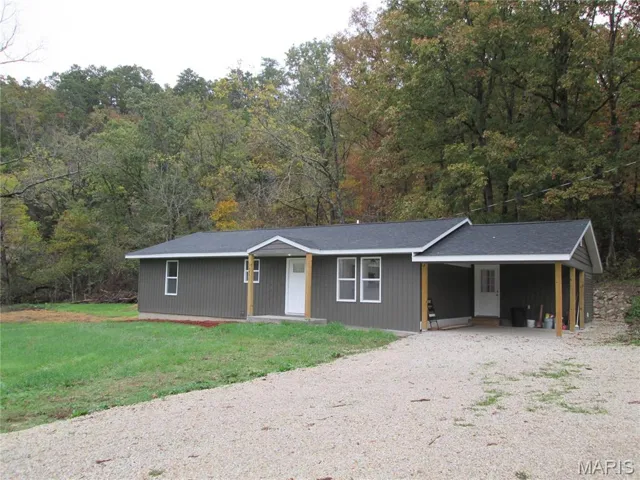 View of front of property with gravel driveway, an attached carport, a front yard, and a shingled roof