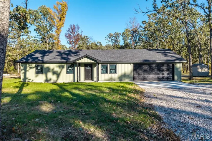 View of front facade featuring driveway, roof with shingles, a front lawn, and an outbuilding