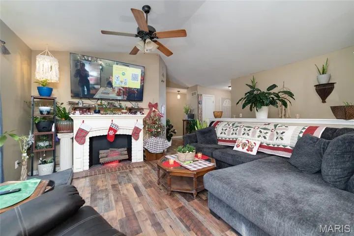 Living area with hardwood / wood-style flooring, a brick fireplace, lofted ceiling, and a ceiling fan