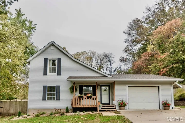 Traditional-style house with a porch, an attached garage, driveway, and roof with shingles