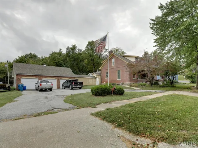 View of front of home featuring a garage, a front lawn, brick siding, and an outbuilding