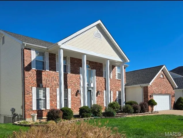 Neoclassical home with a porch, brick siding, a front lawn, and an attached garage