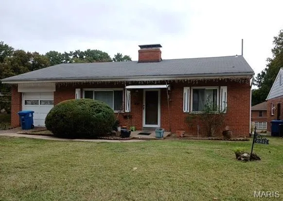 View of front of property with a front yard, a garage, a chimney, and brick siding