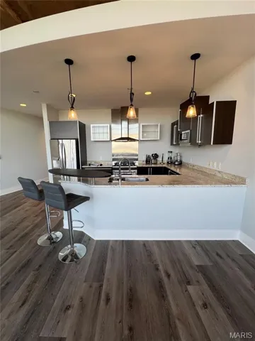 Kitchen with a peninsula, hanging light fixtures, dark wood finished floors, appliances with stainless steel finishes, and wall chimney range hood