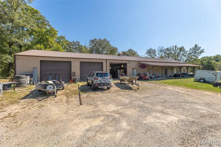 View of front of property featuring a garage, dirt driveway, a chimney, and a metal roof