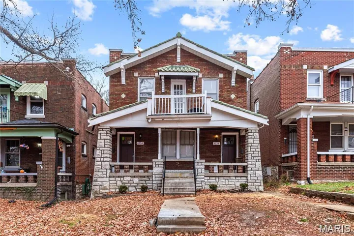 View of front of property with brick siding, covered porch, a chimney, a balcony, and stone siding