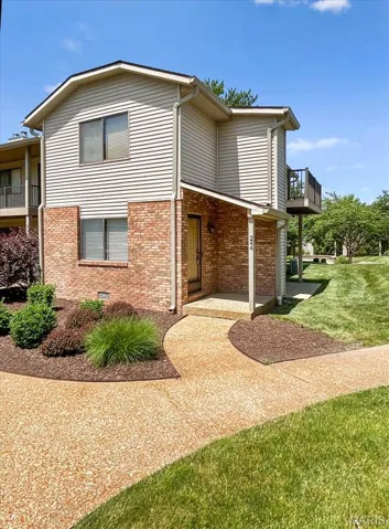 View of front of home with brick siding, a balcony, and a front yard