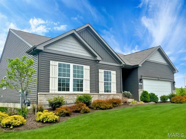 View of front facade featuring stone siding, board and batten siding, a front yard, and a garage