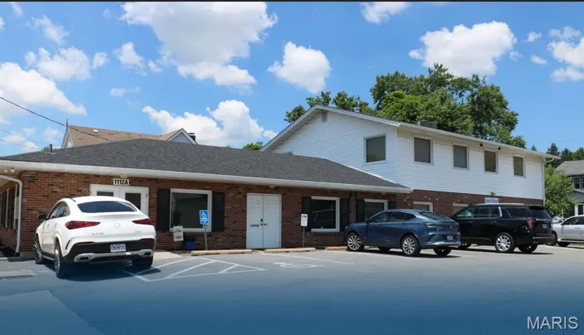 View of front of home featuring brick siding, roof with shingles, and uncovered parking
