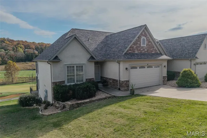 View of front of home with stucco siding, a front lawn, driveway, and roof with shingles