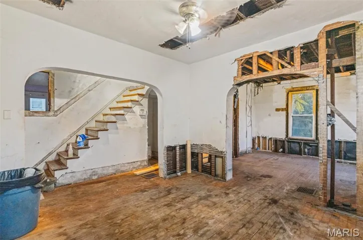 Unfurnished living room featuring stairs, arched walkways, ceiling fan, and hardwood / wood-style flooring